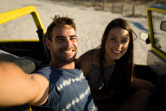 Happy caucasian couple sitting in beach buggy by the sea taking selfie - Powered by Adobe