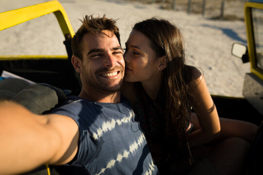 Happy caucasian couple sitting in beach buggy by the sea taking selfie - Powered by Adobe