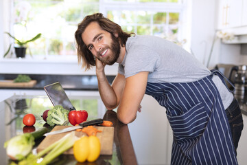 Portrait of caucasian man in kitchen wearing apron and using tablet