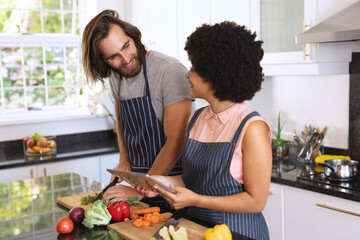 Happy diverse couple in kitchen using tablet and preparing food