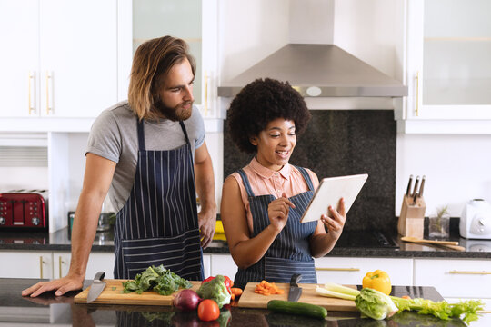 Happy Diverse Couple In Kitchen Smiling And Using Tablet
