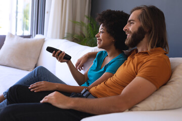 Happy diverse couple sitting on sofa embracing and watching tv
