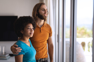 Happy diverse couple looking through window embracing and smiling