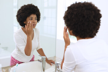 Fototapeta premium African american woman standing in bathroom applying face cream