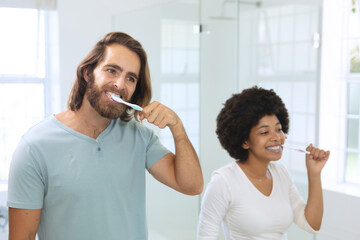 Diverse couple standing in bathroom brushing teeth