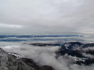 Beautiful scenic winter view of hills and mountains in Gorenjska, Slovenia covered by mist and fog and Kamnik-Savinja alps behind in clouds