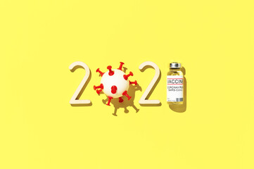 The 2021 - year of mass vaccination against COVID-19 of world population, concept of victory over coronavirus. Top view of number 2021, ampoule, and ball in form virus on bright yellow background