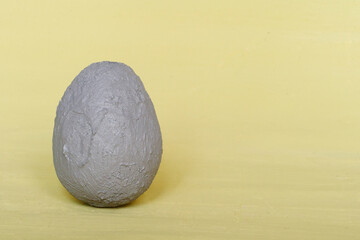 A dark gray decorative egg on a light yellow background. Happy Easter background. Minimal Easter.
