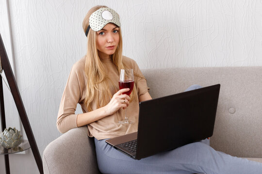 Emotional Woman With A Bandage On Her Head And A Glass Of Wine On The Sofa With A Laptop