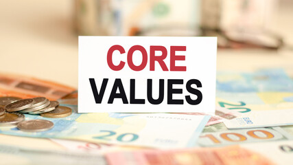 on the table are bills, a coins and a sign on which it is written core values, finance and economics concept