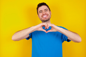 young handsome caucasian man wearing blue t-shirt against yellow background looking at the camera blowing a kiss with hand on air being lovely and sexy. Love expression.