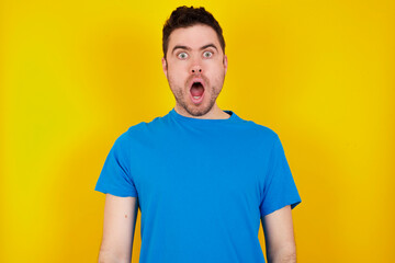Obraz premium Frustrated young handsome caucasian man wearing blue t-shirt against yellow background feels puzzled and hesitant, shrugs shoulders in bewilderment, keeps mouth widely opened, doesn't know what to do.