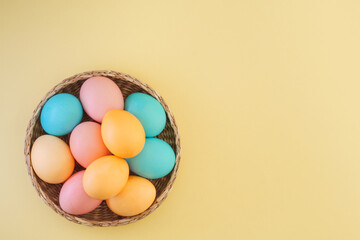 Fototapeta na wymiar Many Easter colored eggs in pastel colors in a wicker basket on a yellow background with copy space, top view, flat layout