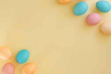 Obraz premium Easter trending yellow background with colorful eggs painted in pastel shades of blue, pink and yellow. Space for text, top view, flat lay. Easter composition