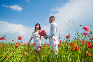 Happy couple breathing fresh air in a field with red poppy flowers, romantic date