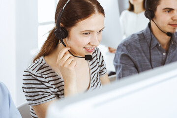 Casual dressed young woman using headset and computer while talking with customers online. Group of operators at work. Call center, business concept