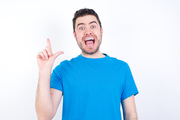 young handsome caucasian man wearing blue t-shirt against white background holding finger up having idea and posing
