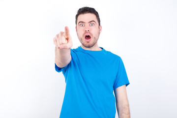 young handsome caucasian man wearing blue t-shirt against white background Pointing with finger surprised ahead, open mouth amazed expression, something on the front.