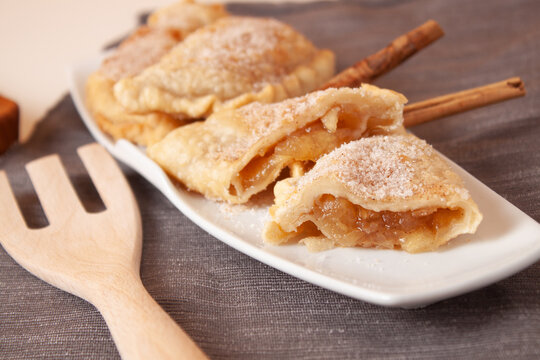 Vista de un plato de empanadillas rellenas de crema de manzana con dos ramas de canela y un tenedor de madera.