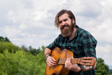 brutal caucasian hipster with beard in shirt play acoustic guitar, vocal