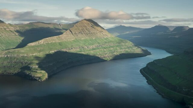 Time lapse of sunset and moving shadows in the fjord at viewpoint Hvithamar with moving clouds over mountains and ocean, Funningur Gjogv Faroe Islands

