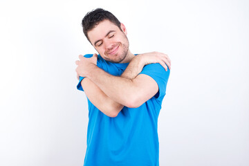 young handsome caucasian man wearing blue t-shirt against white background Hugging oneself happy and positive, smiling confident. Self love and self care