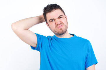 Obraz premium young handsome caucasian man wearing blue t-shirt against white background being confused and wonders about something. Holding hand on her head, uncertain with doubt. Pensive concept.