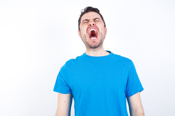 young handsome caucasian man wearing blue t-shirt against white background angry and mad screaming...