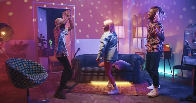 Mixed-races young people having fun dancing at home party. Friends socializing, youth dance moving rhythmically together. Stylish guys and woman dance in living room in disco lights. Fun concept
