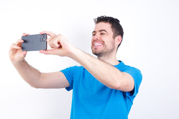 young handsome caucasian man wearing blue t-shirt against white background taking a selfie to post...