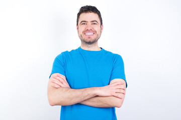 Self confident serious calm young handsome caucasian man wearing white t-shirt against white background  stands with arms folded. Shows professional vibe stands in assertive pose.