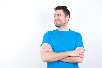 Pleased young handsome caucasian man wearing white t-shirt against white background keeps hands crossed over chest looks happily aside