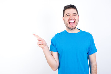 young handsome caucasian man wearing white t-shirt against white background laughs happily points away on blank space demonstrates shopping discount offer, excited by good news or unexpected sale.