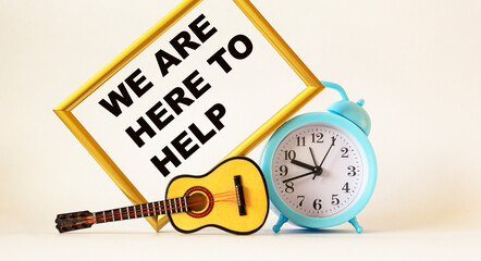 We're here to help text on photo frame, near miniature guitar and alarm clock .Business concept