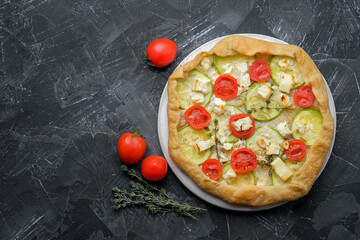 Rustic homemade galette with cheese and vegetables on a dark background top view with copy space.