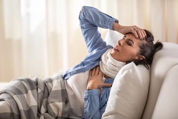 Fototapeta premium Woman suffers from symptoms such as lungs pain and headache while resting on sofa at home