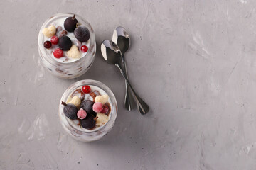 Granola crispy honey muesli with frozen berries, cottage cheese and natural yogurt in two glass jars on light gray background. View from above. Copy space