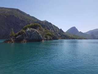 Seascape. Bay with green water against the background of mountains covered with forest on a cloudless sunny day.