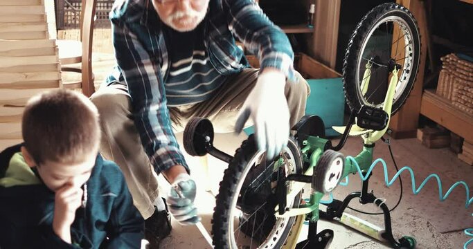 Old man shows his grandson how to inflate a tire on a bicycle.