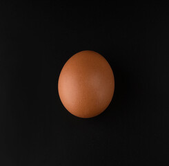 Chicken egg with brown shell on black background