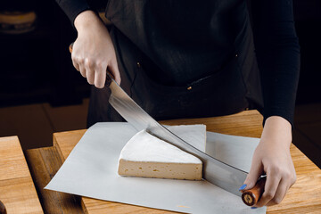 Brie soft white cheese from cow milk. Slicing brie on the wooden table. Organic delicious food