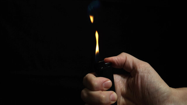 Hand burning flame with a lighter in the dark, black night background, portable device used to create a flame