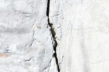 An old white brick wall with a large fracture and a crack.