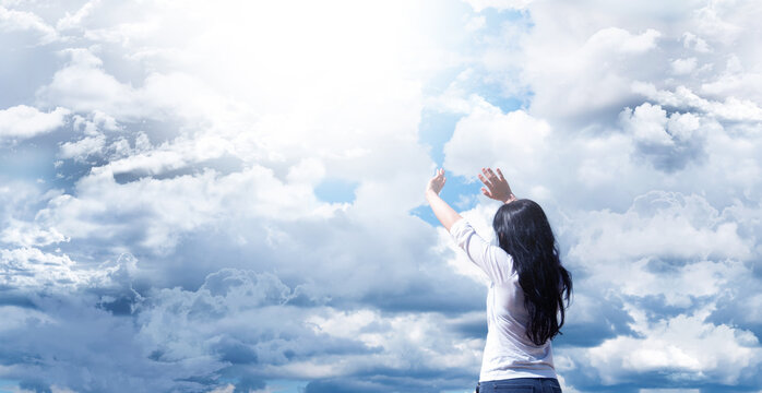 Young girl with raised arms. Against a background of blue sky and clouds. Joy. Prayer and worship to God.
