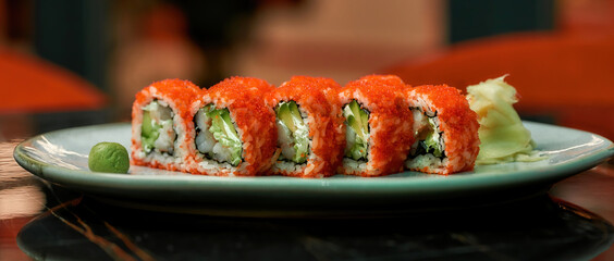 Closeup of red sushi rolls with caviar, seafood, wasabi and ginger on a white plate on table of Japanese restaurant