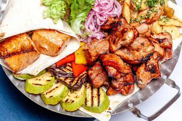 Mixed grill meat fried vegetables and grilled salmon fish fillets decoration in warm dish. Assorted delicious grilled kebab served with herbs on platter. Restaurant menu barbecue plate Bbq party meal