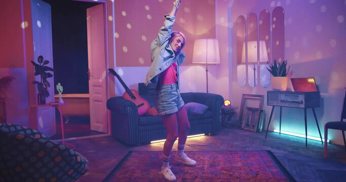 Happy young Caucasian stylish beautiful woman listening to music in headphones and dancing making rhythmic moves in living room in disco ball light in house, retro style, having fun, vintage concept