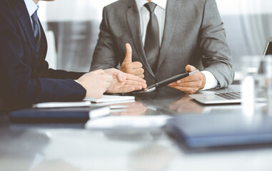 Unknown businessman using tablet computer and working together with his colleague while sits at the glass desk in modern office. Teamwork and partnership concept