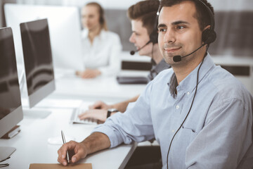 Fototapeta premium Call center. Group of casual dressed operators at work. Adult businessman in headset at customer service office. Telesales in business