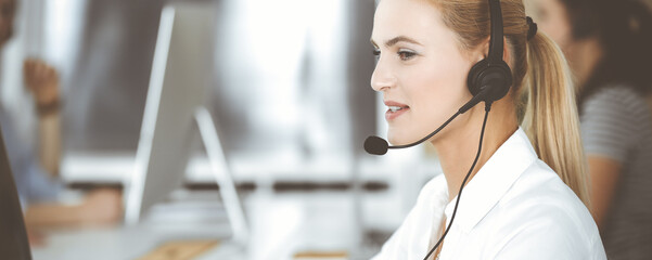 Blonde business woman using headset for communication and consulting people at customer service...